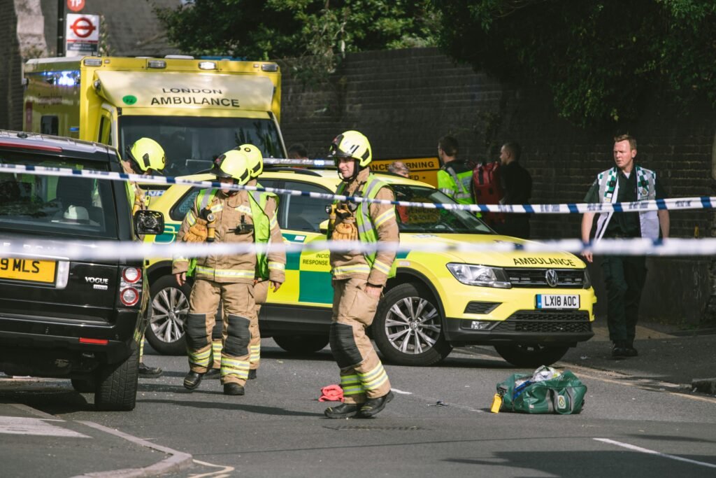 Firefighters and paramedics at a London street accident, featuring emergency vehicles and police tape.