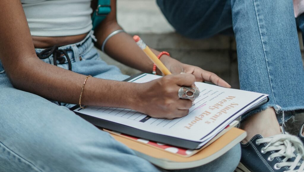 An African American student writes a report outdoors, concentrating on her work.